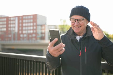Portrait of senior man using mobile phone while standing on the bridge