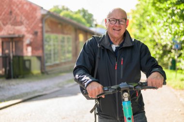 Portrait of a smiling senior man riding a electric kick scooter in city looking at camera