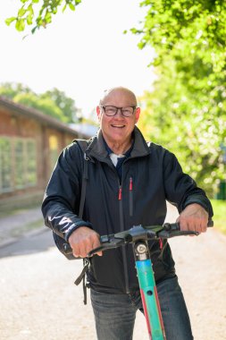 Portrait of a smiling senior man riding a electric kick scooter in city looking at camera
