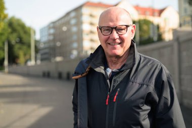Portrait of a Nordic smiling bald senior man with glasses wearing a sport jacket outdoors