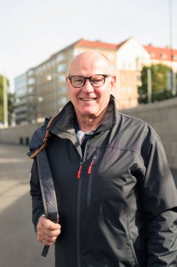 Portrait of a Nordic smiling bald senior man with glasses wearing a sport jacket outdoors