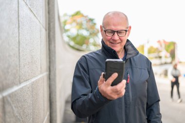 Smiling mature man with mobile phone in his hands outdoors.