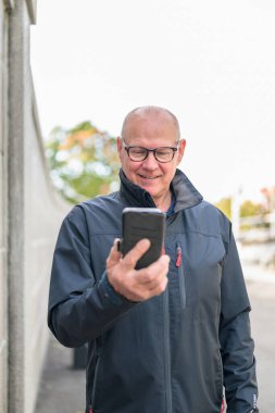 Smiling mature man with mobile phone in his hands outdoors.
