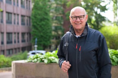 Portrait of a smiling senior man walking in the city with a backpack