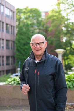 Portrait of a smiling senior man walking in the city with a backpack looking at camera
