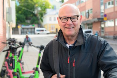 Portrait of a smiling bald senior man ready to ride an electric kick scooter in the city