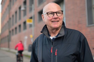 Portrait of a smiling senior man with eyeglasses waiting at a bus stop in the city alone