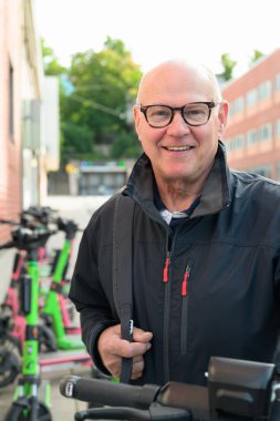 Portrait of a smiling bald senior man ready to ride an electric kick scooter in the city