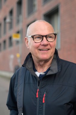 Portrait of a smiling senior man with eyeglasses waiting at a bus stop in the city alone