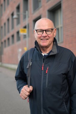 Portrait of a smiling senior man with eyeglasses waiting at a bus stop in the city alone