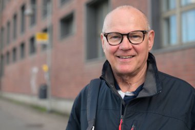 Portrait of a smiling senior man with eyeglasses waiting at a bus stop in the city alone