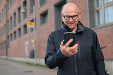 Handsome mature man using his smart phone in an urban context waiting for public transportation bus