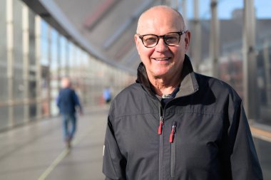 Portrait of a bald senior man wearing glasses and a jacket in train station bridge
