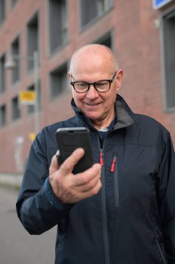 Handsome mature man using his smart phone in an urban context waiting for public transportation bus