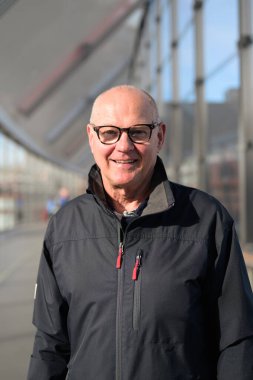 Portrait of a bald senior man wearing glasses and a jacket in train station bridge