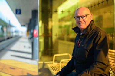 Portrait of a senior man sitting on a bench at a train station outdoors
