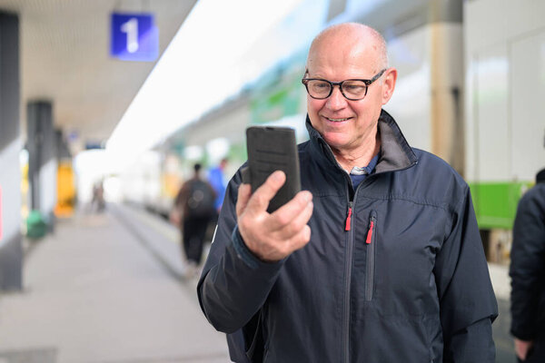Portrait of Scandinavian senior man using mobile phone at the train station.