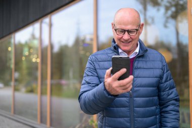 Portrait of a bald senior Scandinavian man using a mobile phone in the city
