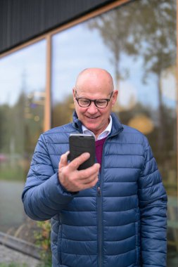 Portrait of a bald senior Scandinavian man using a mobile phone in the city