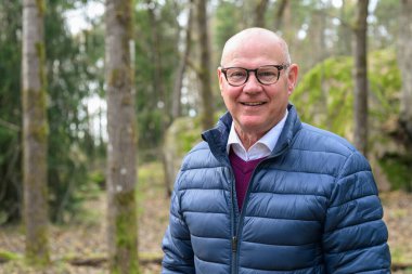 Portrait of a happy senior man smiling in the woods with eyeglasses
