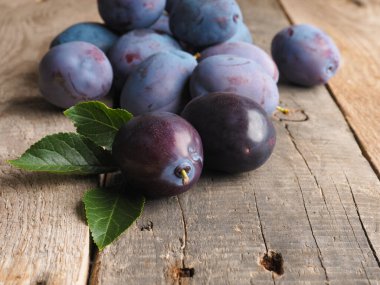 Tasty organic plums on a rustic wooden kitchen table, healthy fruits or seasonal food concept background clipart