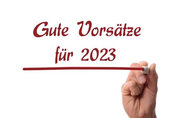 Hand with a red felt-tip pen writes the German words Good Intentions for 2023 on a glass surface, business concept