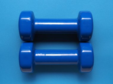 Mavi arka planda iki mavi dambıl, sağlık hizmeti veya fitness konsepti