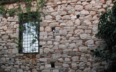 Düzensiz tuğlaları ve doğal dokuyu ve mimariyi yansıtan penceresi olan eski bir taş duvar.