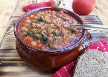 Ahşap masa arkasında domates soslu fırında fasulye kasesi.