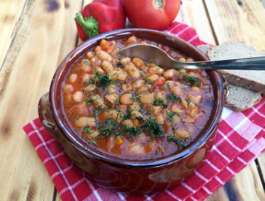 Ahşap masa arkasında domates soslu fırında fasulye kasesi.