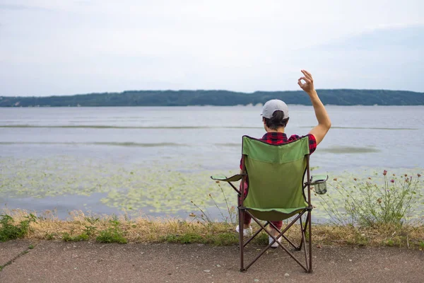 Man rests on a camping chair and looks out over the lake on a sunny day
