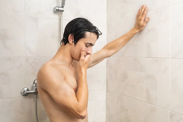 Man suffering from anxiety in the shower. Drops of water falling on him from the shower head. Man suffering from anxiety