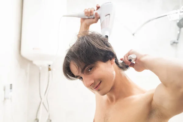 Man styling his hair with a blow dryer after a shower