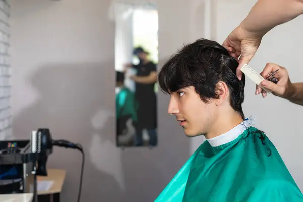 A young man in the salon. Hairdresser makes a fashionable haircut with scissors and comb