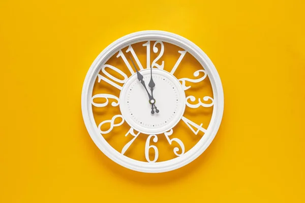 Modern white clock with a circle on a yellow wall background, five to twelve on the clock. Elegant clock, combination of white and yellow colors