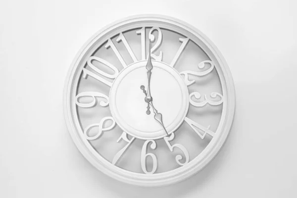 Modern white clock with a circle on a white wall background, five o\'clock on the clock