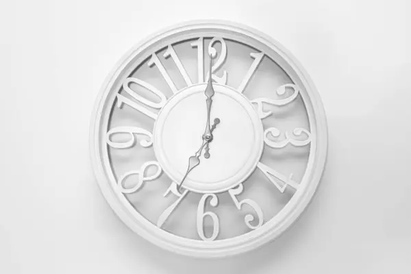 Modern white clock with a circle on a white wall background, seven o\'clock on the clock