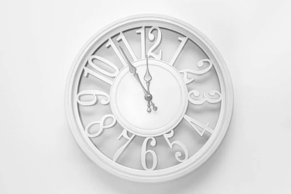 Modern white clock with a circle on a white wall background, five to twelve on the clock