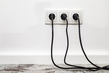 Üç beyaz priz beyaz bir duvara monte edilmiş, üç siyah buji takılmış, ön görünüm.
