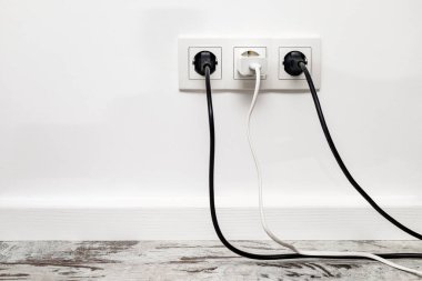 İki siyah buji ve beyaz telefon adaptörüyle beyaz bir duvara üç beyaz priz takılmış. Önden görünüm.