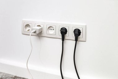 Beyaz beş kanallı prizler beyaz bir duvara monte edilmiş. İki siyah buji ve beyaz bir telefon adaptörü var..