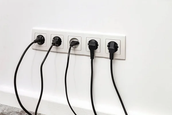 白色的五边形电源插座安装在五根黑色插头的白色墙壁上 出口塞满了黑线 — 图库照片