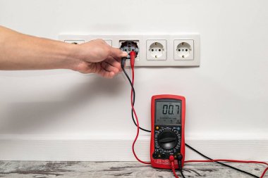 Beyaz duvara beş kanallı bir priz takıldı. Çoklu metresi olan adam mevcut voltajı ölçer.
