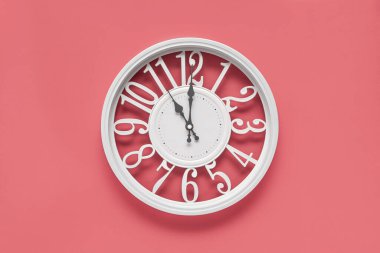 Pembe duvar zemininde bir dairesi olan modern beyaz saat, saat 11 yönünde. Barbekü tarzında zarif bir saat, beyaz ve pembe renklerin kombinasyonu