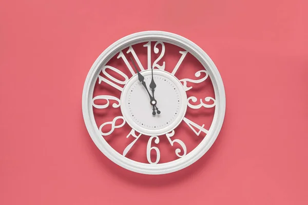 Modern white clock with a circle on a pink wall background, five to twelve on the clock. Elegant clock in the barbie style, combination of white and pink colors