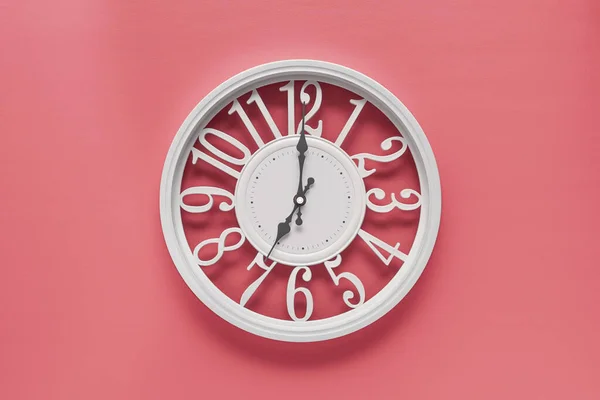 Modern white clock with a circle on a pink wall background, seven o'clock on the clock. Elegant clock in the barbie style, combination of white and pink colors