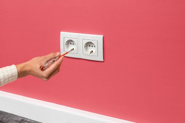 İnsan eli prize takılı bir tornavida tutuyor. Pembe duvarda beyaz çift soket, yan görüş.