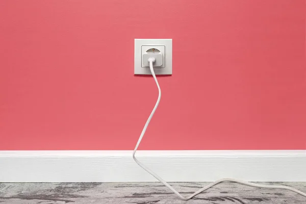 White outlet installed on the pink wall with inserted phone adapter, front view.