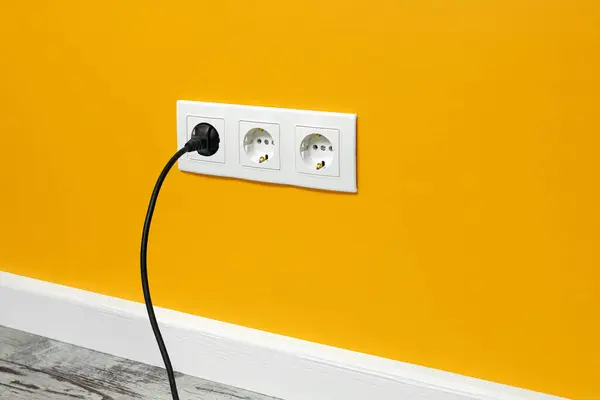 白色三重插座安装在黄墙上 插上黑色插头 — 图库照片