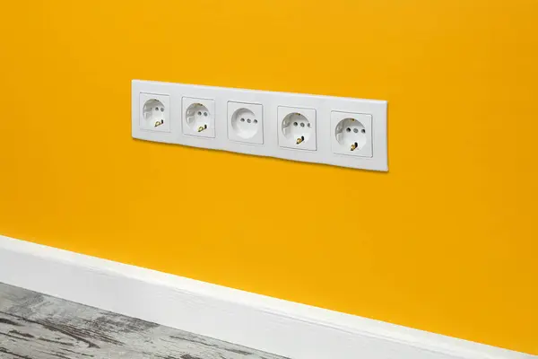 White five-way wall power socket installed on the yellow wall, side view.